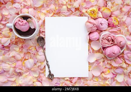 Background of pink rose buds and petals with blank card in centre and a cup of tea with rose and tea spoon. Flat lay, overhead view. Mother's Day, St. Stock Photo