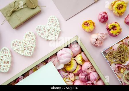 Valentine's Day composition. Flat lay of white hearts, handmade gift boxes, craft paper, envelope, rose buds on pink background. Top view, Copy space. Stock Photo