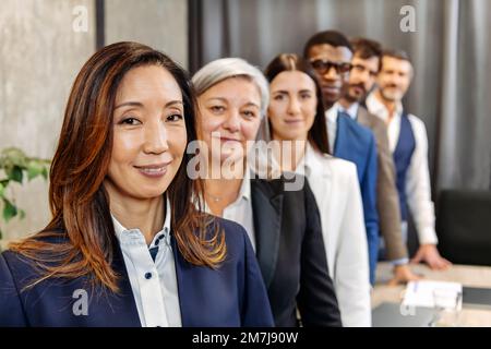 Team of diverse colleagues in formal wear standing in row and looking at camera in modern office Stock Photo