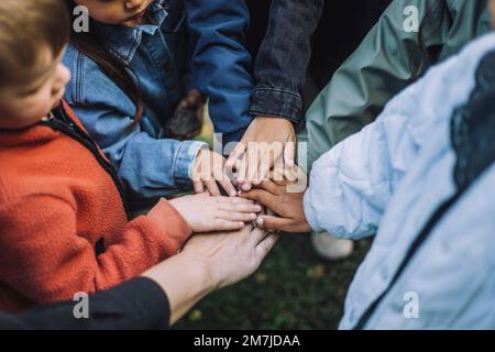 Playful multiracial preschool students stacking hands with teacher in park Stock Photo