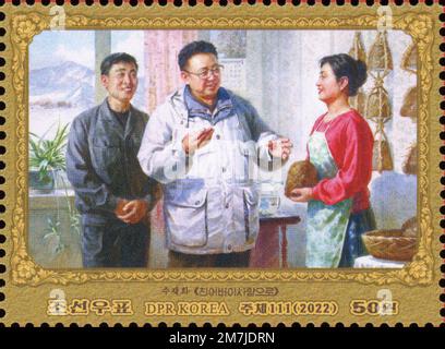 2022 North Korea stamp. 80th Anniversary of the Birth of Kim Jong Il, 1942-2011 Painting of the leader visiting home and giving culinary advice. Stock Photo