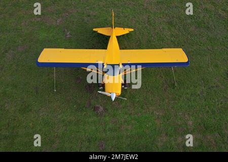 small yellow plane used for short trips seen from above parked on a green field Stock Photo