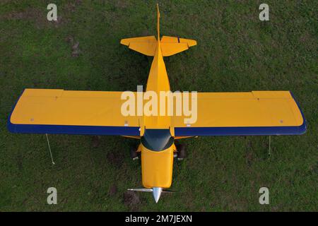small yellow plane used for short trips seen from above parked on a green field Stock Photo