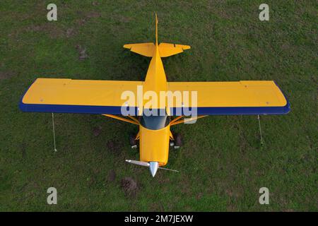 small yellow plane used for short trips seen from above parked on a green field Stock Photo