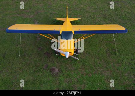 small yellow plane used for short trips seen from above parked on a green field Stock Photo