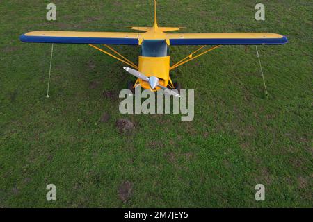 small yellow plane used for short trips seen from above parked on a green field Stock Photo