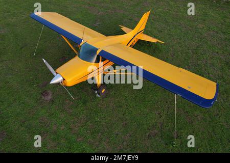 small yellow plane used for short trips seen from above parked on a green field Stock Photo