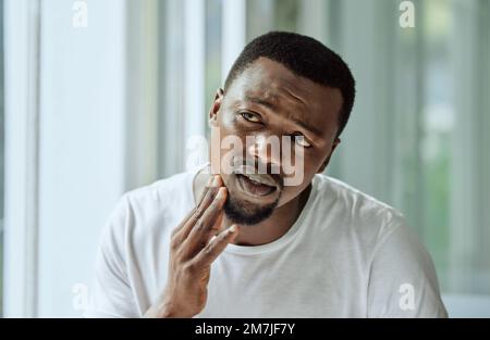 Sad, aesthetic and anxiety of black man with acne confused with face analysis in home bathroom mirror. Unhappy skincare man checking pimple problem in Stock Photo
