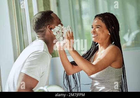 Shave, playing and funny with a black couple laughing or joking together in the bathroom of their home. Love, shaving and laughter with a man and Stock Photo
