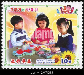 2021 North Korean postage stamp featuring children engaged in creative arts, drawing, and origami. DPRK philatelic collection. Stock Photo