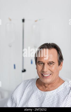 Positive grey haired patient looking at camera in blurred hospital ward,stock image Stock Photo