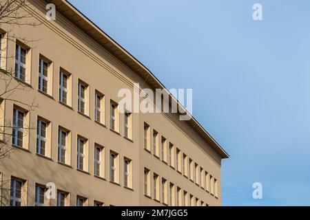 Corner of a building against blue sky. Beige plaster, simple, linear cornice and row of windows. Stock Photo