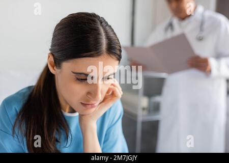 Displeased patient looking down near blurred doctor in hospital ward,stock image Stock Photo