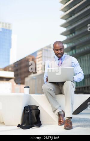 Young adult African American businessman working outdoors with laptop computer. Space for text. Stock Photo