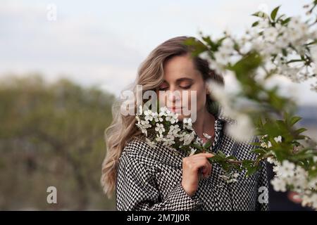 Beautiful woman smell flowers cherry tree. Female model in blooming garden in spring Stock Photo