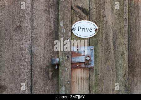 Closeup of old weathered wooden fence door with rusty metal lock handle and white oval private property sign with text privé in dutch. Stock Photo