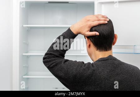 Rear view of a confused young man looking at food in refrigerator with copy space. Stock Photo