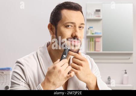Young man in a bathrobe using a beard trimmer inside bathroom Stock Photo