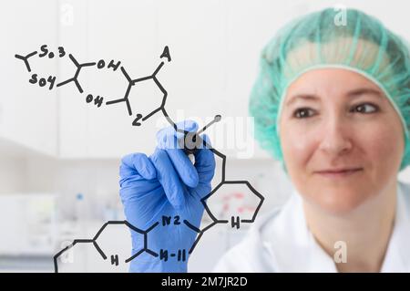 Shot of a focused young female scientist solving equations on a glass wall in a laboratory Stock Photo