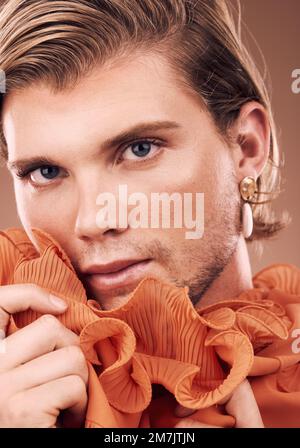 Lgbtq, fashion and portrait of man with makeup, beauty and creative orange clothes on studio background. Transgender, face and queer model with Stock Photo