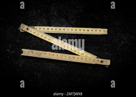 Wooden measuring rules with clear markings are laid out in an angled position on a dark background, highlighting their measurement details. Stock Photo