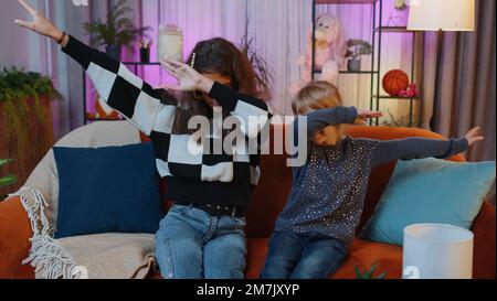 Teenage child and little sister kid girls wearing stylish sunglasses listening music and dancing disco fooling around having fun, relaxing on party. Siblings children or best friends at home play room Stock Photo