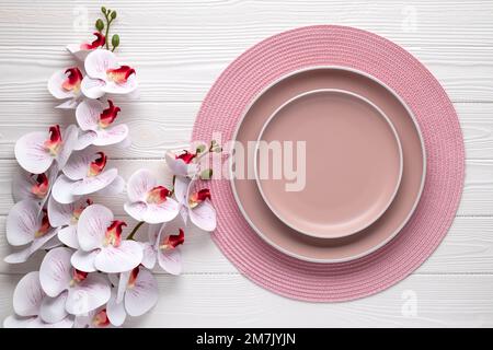 Empty plates and round pink napkin on white wooden table. Place setting with beige dishes. Dining ware. Festive card or menu template with copy space, Stock Photo