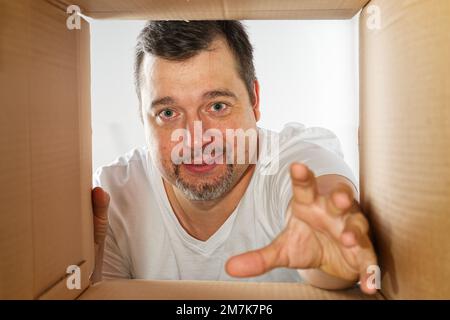 Happy man unpacking, opening carton box and looking inside. Man smiling unpacking and carton box Stock Photo