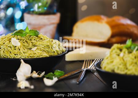 Selective focus of two plates of pesto spaghetti pasta with fresh basil leaves and parmesan cheese over a black rustic wood table. Stock Photo