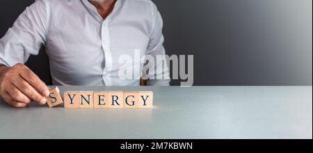 man posing wooden blocks with the word synergy , concept of team work and partnership . Stock Photo