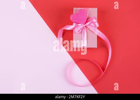 Happy Valentine's Day, Mother's Day and birthday greeting card. Knitted pink heart and gift box with a satin ribbon bow on a pink and red background Stock Photo