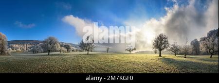 Winter landscape panorama, hoarfrost on open meadow, blue sky with dramatic clouds and sun rays Stock Photo