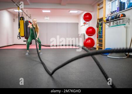 Young woman with perfect body doing crossfit exercises with a rope in the gym. Stock Photo