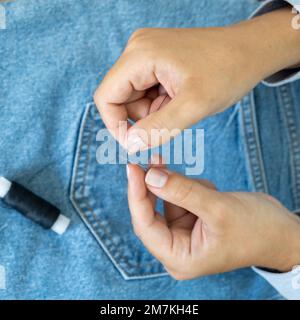 Hands of a seamstress threading a needle on the background of jeans Stock Photo