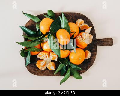 Fresh ripe tangerines and leaves on wood brown board on beige background, flat lay. Citrus fruit top view Stock Photo