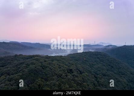 Distant early morning sun lights sky pink over misty hilly landscape Stock Photo