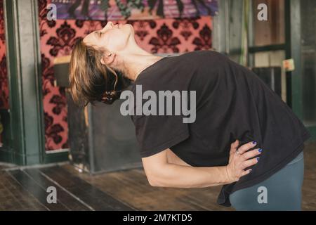 Close-up photo of young adult female yogi and new teacher doing a camel pose (Ustrasana), eyes closed, workout yoga practice Stock Photo
