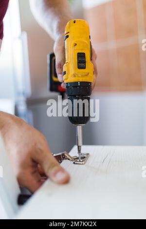 Close up man holding cordless screwdriver machine and screws lie for screwing a screw assembling furniture at home Stock Photo