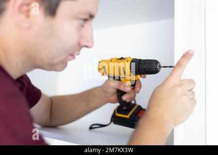 Handyman using screwdriver while installing kitchen cabinets at home Stock Photo