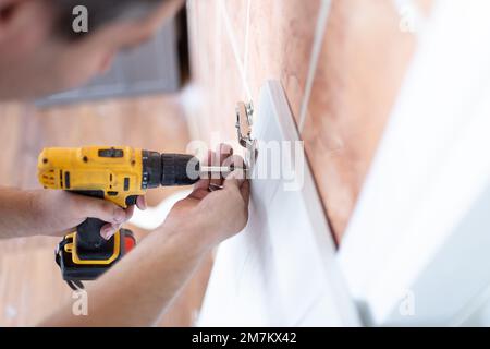Man Assembling Shelf Using Electric Drill Tool At Home. Male Housework And House Furnishing. Handyman Fixing Wooden Cabinet During Renovation Stock Photo
