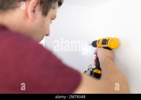 Man assembling white kitchen wooden furniture a home by using cordless screwdriver. Space for copy. Stock Photo