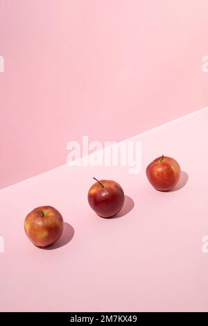 Three fresh red apples on pink background. Minimal fruit concept. Stock Photo