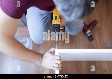 Man installing wooden shelves by using cordless screwdriver Stock Photo