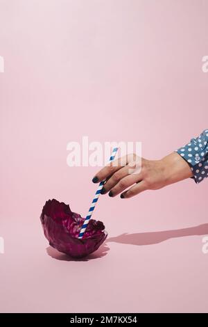 Female hand holding paper straw in leaf of red cabbage. Minimal vegetable concept. Stock Photo