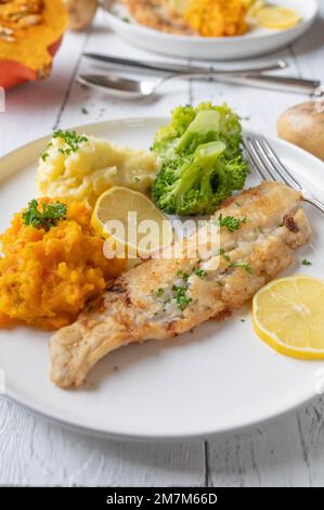 Pan fried  fish fillet with mashed potato, pumpkin puree and broccoli on a plate on white background Stock Photo