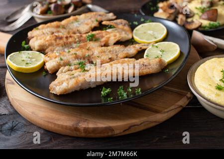 Pan fried fish with creamy polenta and mushrooms fried in butter on a rustic and wooden table for dinner or lunch Stock Photo