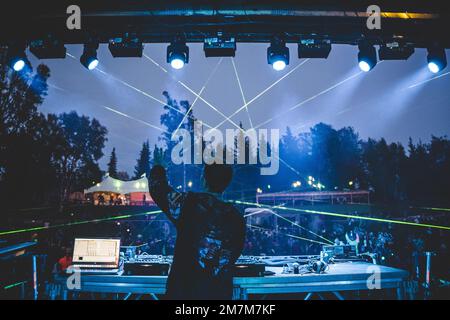 DJ on stage at Music Festival with large crowd, lasers and fun lights Stock Photo