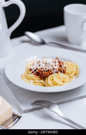 Top view of Bolognese spaghetti with parmesan cheese on top in white plate. Simple white background and decoration. Traditional Italian dish, Mediterr Stock Photo
