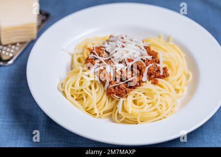 Bolognese spaghetti with parmesan cheese on top in white plate. Simple blue background and decoration. Traditional Italian dish, Mediterranean cuisine Stock Photo