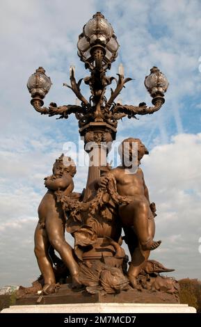 Bronze sculptures at the base of an ornate Art Nouveau street lamp on the landmark Pont Alexandre III bridge in Paris. Stock Photo